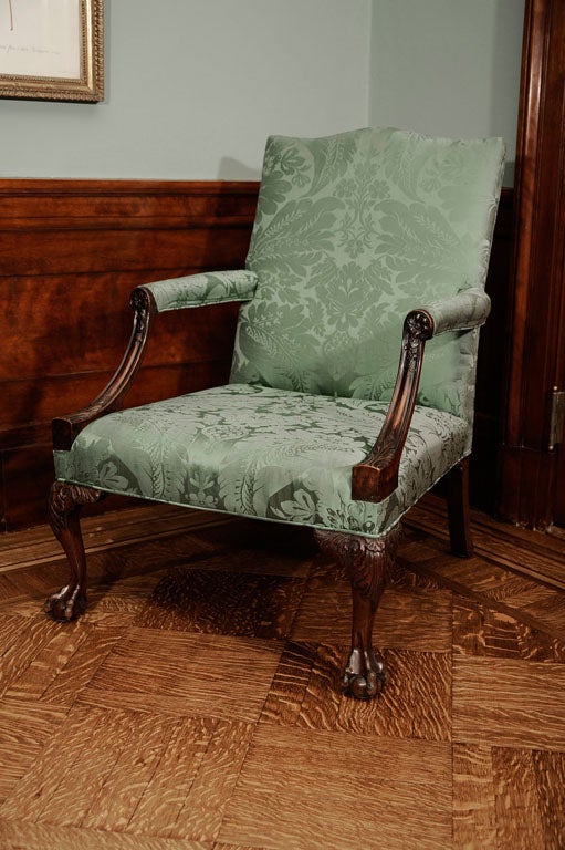 The rectangular upholstered backrest with serpentine top flanked by padded and downswept armrests carved with rosettes and leafy terminals, the upholstered seat raised on cabriole legs carved with acanthus at the knees and ending in ball-and-claw