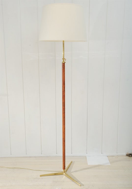 Fabulous and rare Jacques Adnet brass floor lamp sheathed in brown pigskin with exposed top sticthing.  Wonderful exaggerated brass tripod base with tapering legs, and original brass hardware.  Lamp has clever adjustable drop pin locking device