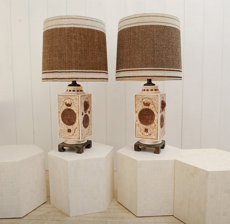 Fabulous pair of white James Mont Chinoiserie style ceramic lamps with hand painted brown patination.  Lamps have unusual unglazed elephant head and medallion motifs on each side.  These lamps retain their original Maria Kipp woven shades and sit