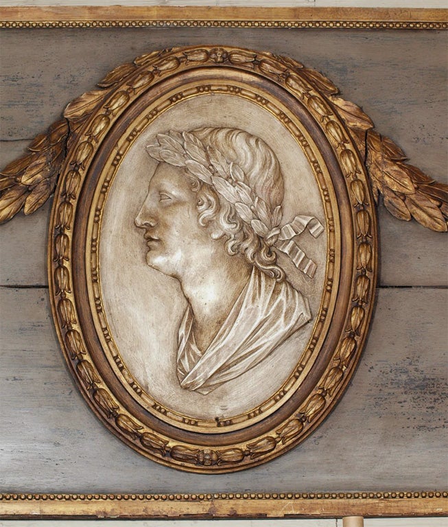 A carved gilt wood oval bearing the profile of a monarch wearing a crown of laurel.  The oval is flanked by matching gilt garland swags.  The gray background is framed in a simple gilt beaded frame.