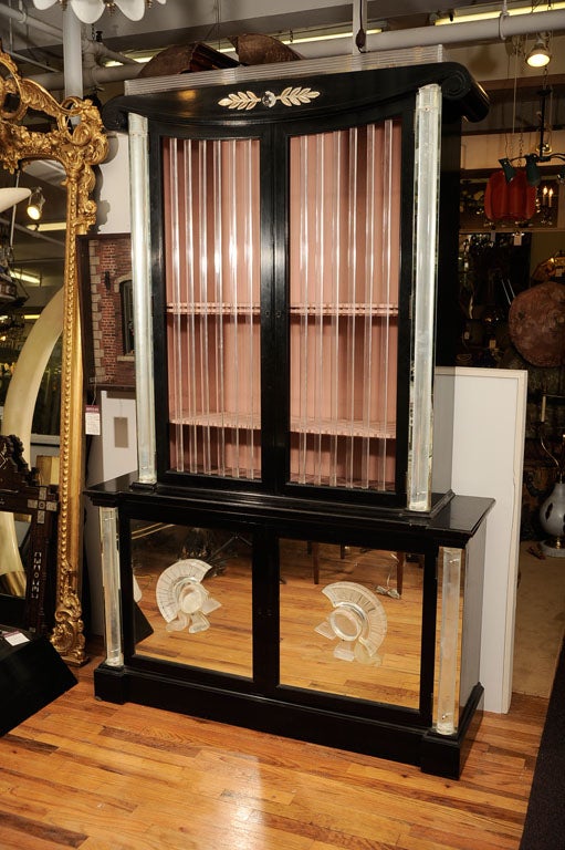 Neoclassical style two-piece cabinet/vitrine with black lacquer finish and lucite and mirror details by Grosfeld House, Circa 1940. The top part features a scrolled top cornice mimicking a classical column with a lucite top and an appliqued lucite
