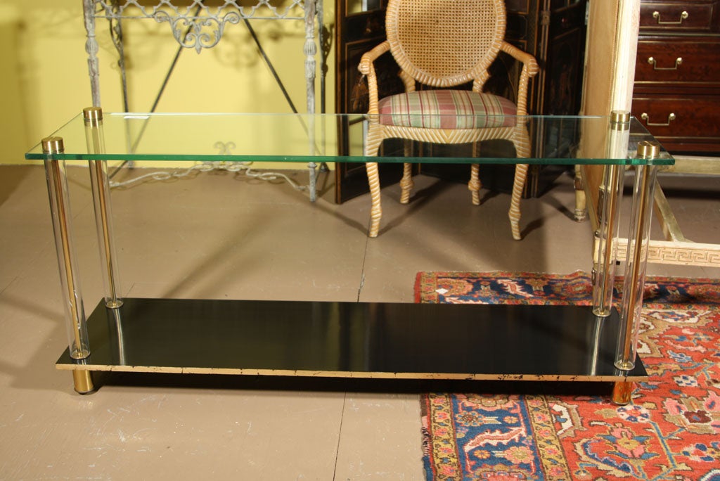 A fine ebonized two-tier console. Shelf is supported by a set of Lucite columns each holding up a glass top shelf. Signed by Maison Jansen. The top and feet of solid bronze.