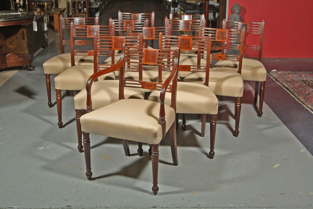 A set of twelve Engish Regency dining chairs consisting of one period armchair and five period sides and six chairs copied in the early 20th century.  The set is mahogany with burlwood panels having satinwood string inlay ending on turned legs.