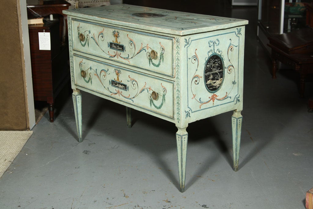 An Italian neoclassical style painted two drawer commode raised on square tapering legs with arabesque decoration and reserved black and white panels of Asian figures.