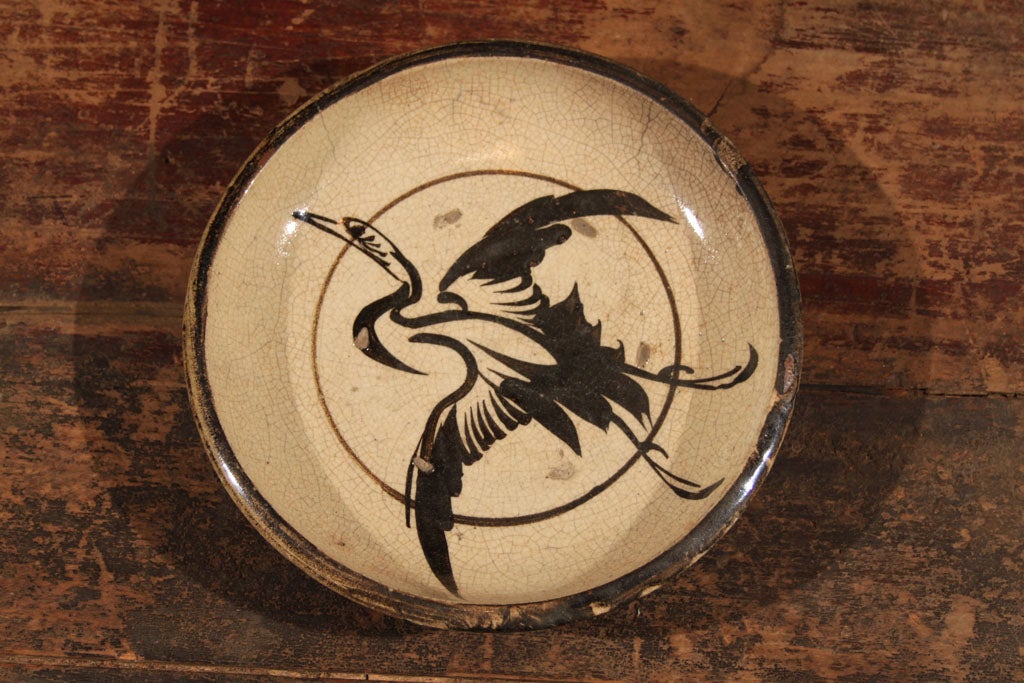 Japanese Seto ware (ishizara) shallow bowl-dish. The cream colored stoneware dish with a translucent glaze, over an iron oxide painting of a flying crane. The painting of the crane executed in quick, bold strokes against a simple circle. The crane