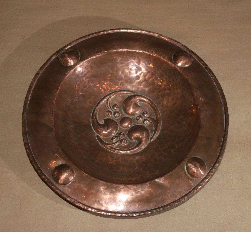 English Arts and Crafts period hammered copper charger with rolled rim, the border with embossed bosses, the centre with Celtic scroll and berry design. Maker unknown.