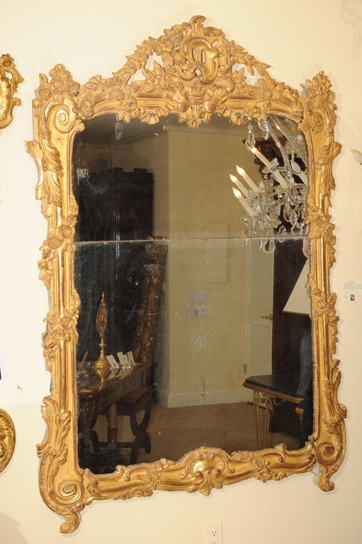 Early 18th Century Period Regence Mirror with Original Double Antiqued Mirror Plate, the Scrolling Sides with Garlands Culminating in Swirled Feet the Top Surmounted the Top Crest with Open Shell Ribbons and Scrolling Vines.  <br />
Circa 1730.