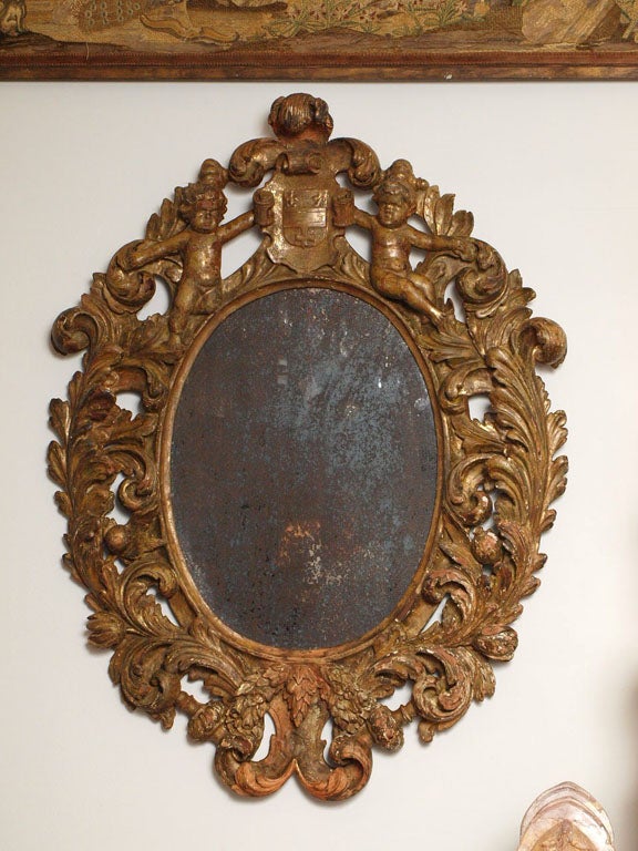 A highly carved mirror with a frame of scrolling foliate design and cartouche of putti flanking a coat of arms.