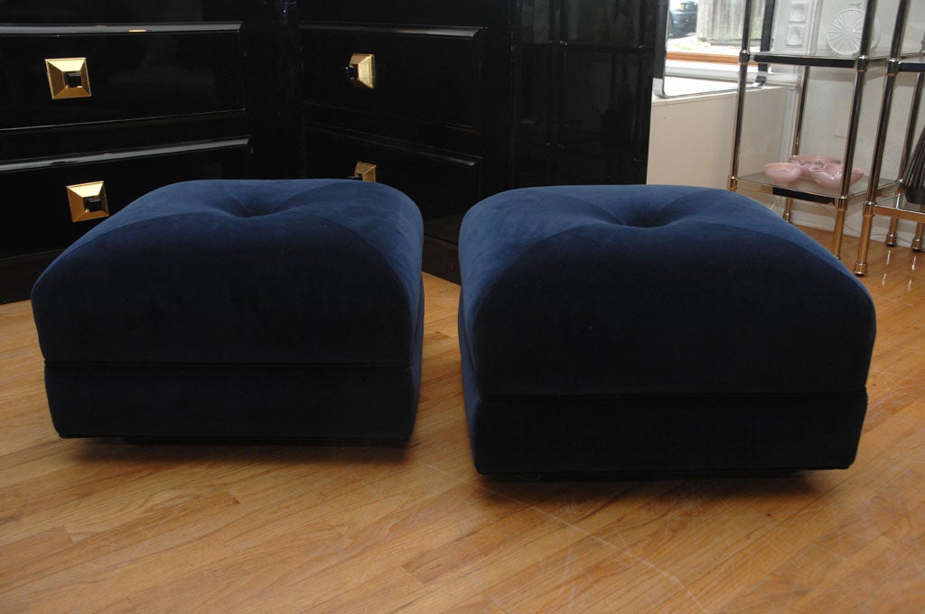 Wonderful Pair of upholstered ottomans in a beautiful Navy blue silk velvet,  they each have a single large center button. <br />
The ottomans are on  brass casters for easy postioning.