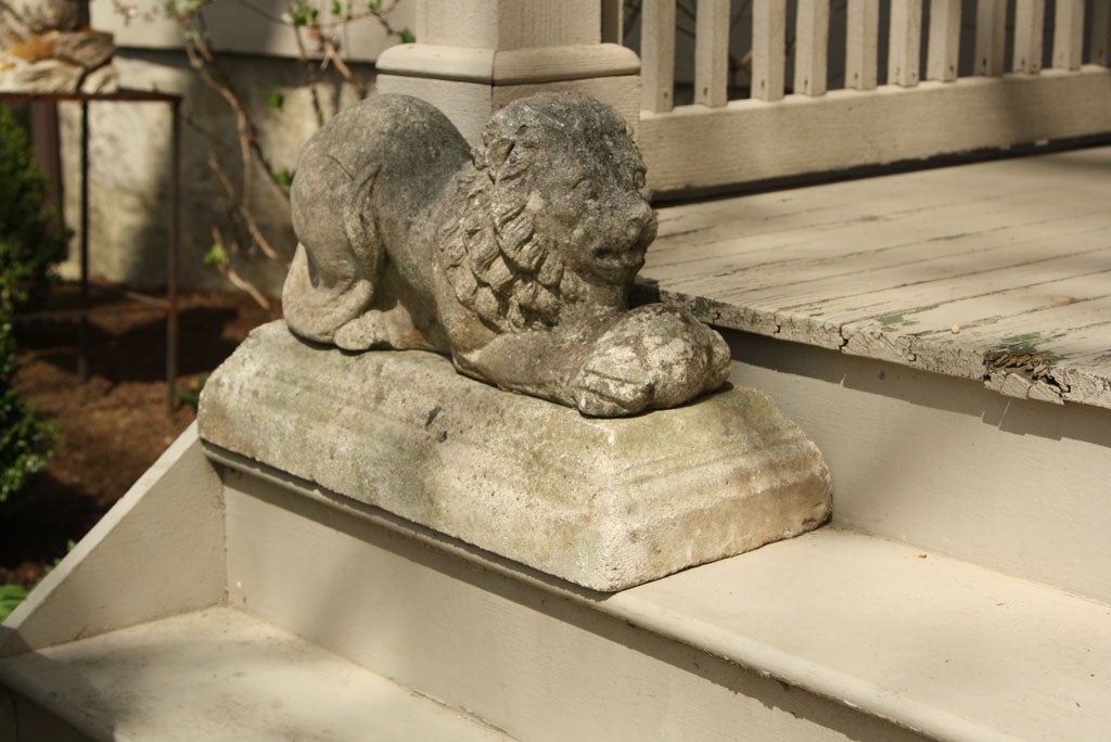 Playful pair of recumbent cast stone lions with balls, reminiscent of Chinese Foo Dogs.  On separate, tiered, original plinths and sporting a mellow weathered surface, these lions are perfect flanking a doorway, garden entrance, or atop a stone wall.