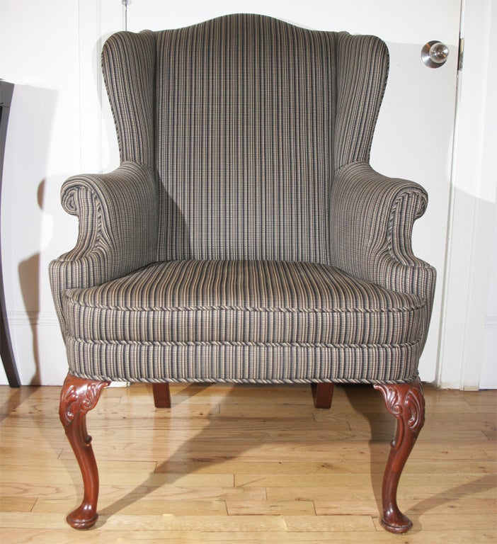 Newly upholstered wing chair in a dark stripe fabric with carved mahogany cabriole legs, a serpentine back, and scrolled arms.
