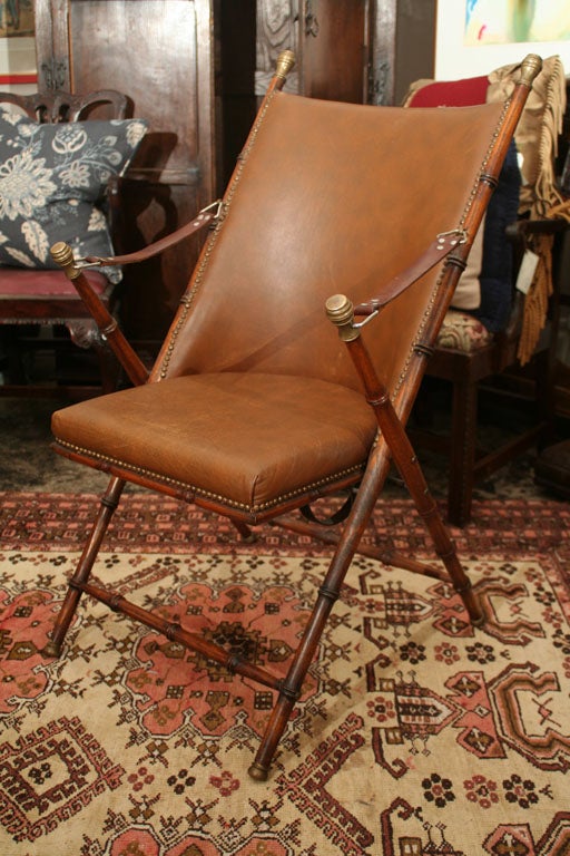 Leather, oak and brass folding campaigne chair.  Turned legs with original nail heads surrounding leather seat and back. Leather straps at arm rests.
