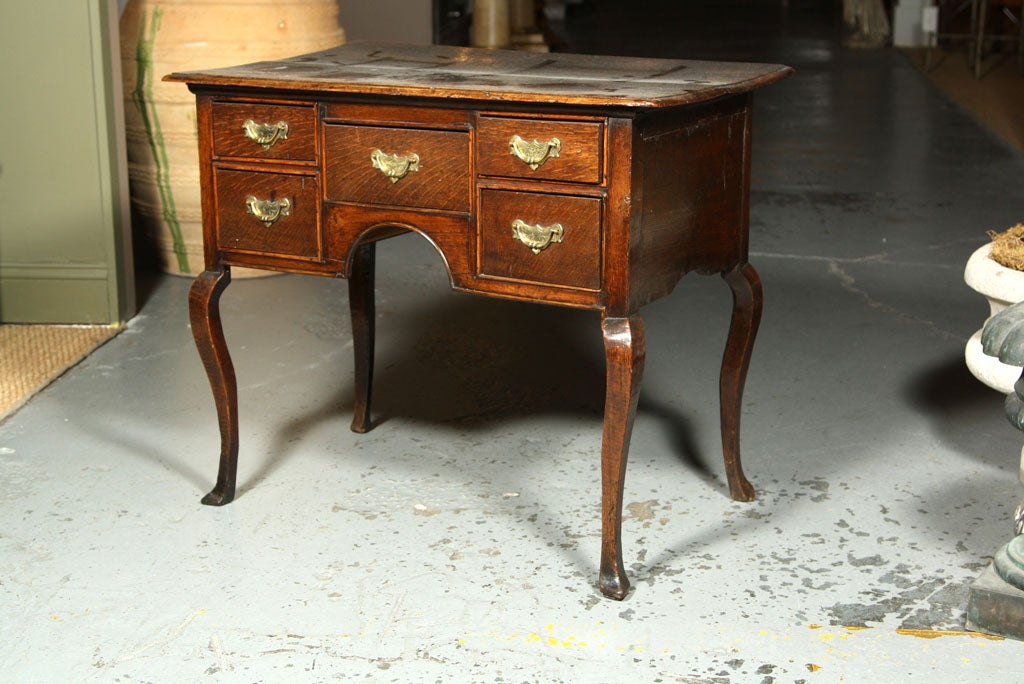 An English oak lowboy, the five drawers with d moulding and retaining the original brasses, shaped apron and standing on cabriole legs.  Drawers possibly relined and lower area of moulding restored.