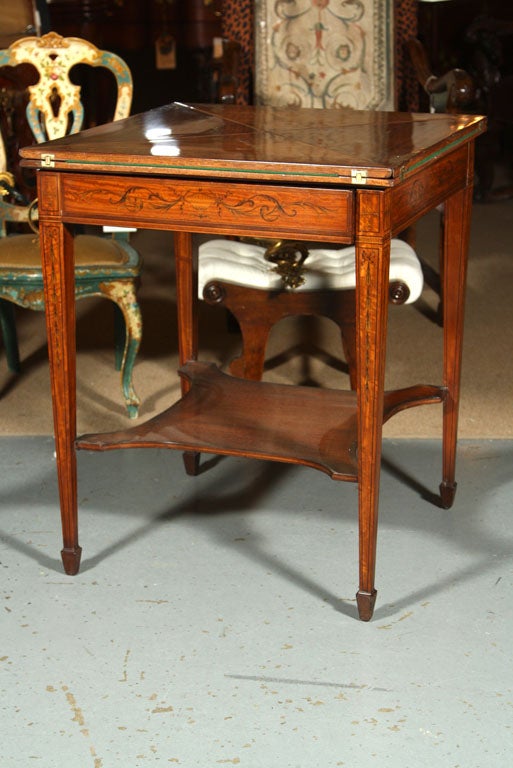 An Edwardian period handkerchief table - a  table  of  the  18th  century  having  a  triangular  top  with  a  triangular  drop  leaf  of  the  same  size - having a single drawer with inlaid bellflower decoration raised on square tapering legs.