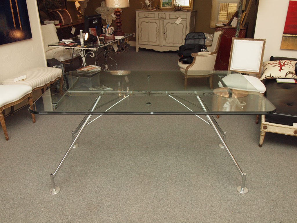 This sleek office table features a clear beveled glass top and aluminum legs.  It is elegant and sophisticated.  Designed by the noted British architect Sir Norman Robert Foster for the Italian manufacturer Tecno in the 1980's, it works equally well