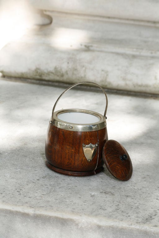 A silver-plated English biscuit barrel, with a shield design on the side, and a porcelain liner and wooden lid. It is side marked in the metal E.R.N.S.