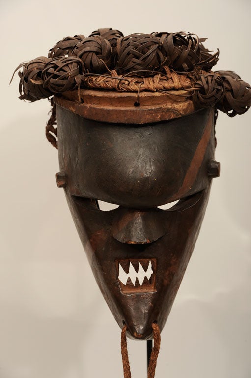 Fiercely visaged mask with bulbous forehead, filed teeth, and original woven fiber head piece. Rakish marking painted in red is an unusual and graphically arresting feature. Measurements include stand.

The Salampsasu tribe was from the Congo, and