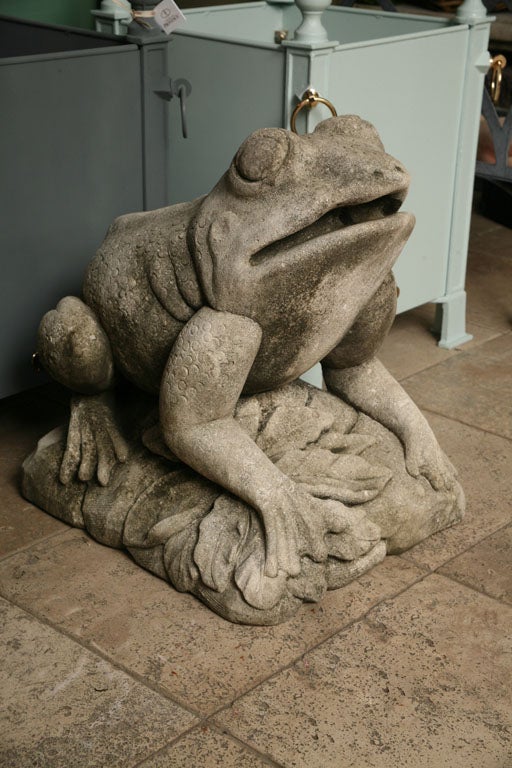 Unusually detailed statue of a garden frog sitting on a rectangular base decorated with leaves.