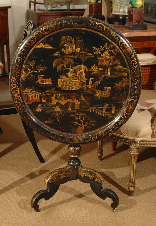 a black lacquer tilt-top table with gilt Chinoiserie pattern and mother-of-pearl accents, top has raised border, tripod base (17