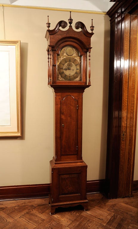 A CHIPPENDALE CARVED WALNUT TALLCASE CLOCK, ADAM BRANT, NEW HANOVER, MONTGOMERY COUNTY, PENNSYLVANIA, CIRCA 1770-90<br />
<br />
The bonnet with broken swan's neck pediment and urn finials above an arched glazed door flanked by turned columns and