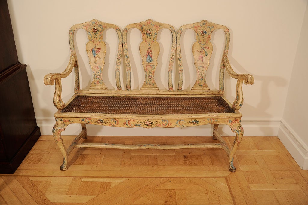 Comprising four single chairs, two armchairs and a settee. The chairs with shaped crest and shaped splat painted with floral decoration and colored scrolls, each splat carrying a depiction of a figure from a Venetian ball. The two armchairs with