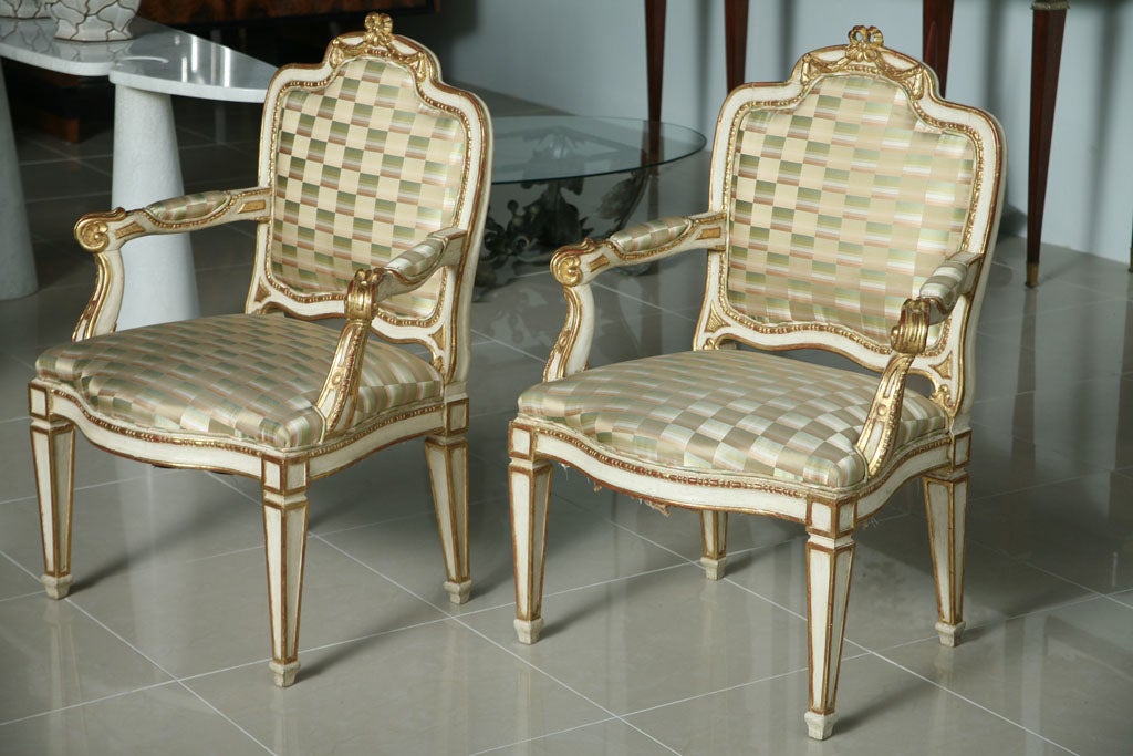 The cartouche shaped back with carved foliate swag with upholstered seat back, above curved arms, the whole resting on square tapering legs termination with a toupie foot, the whole decorated in cream paint and parcel gilding.
