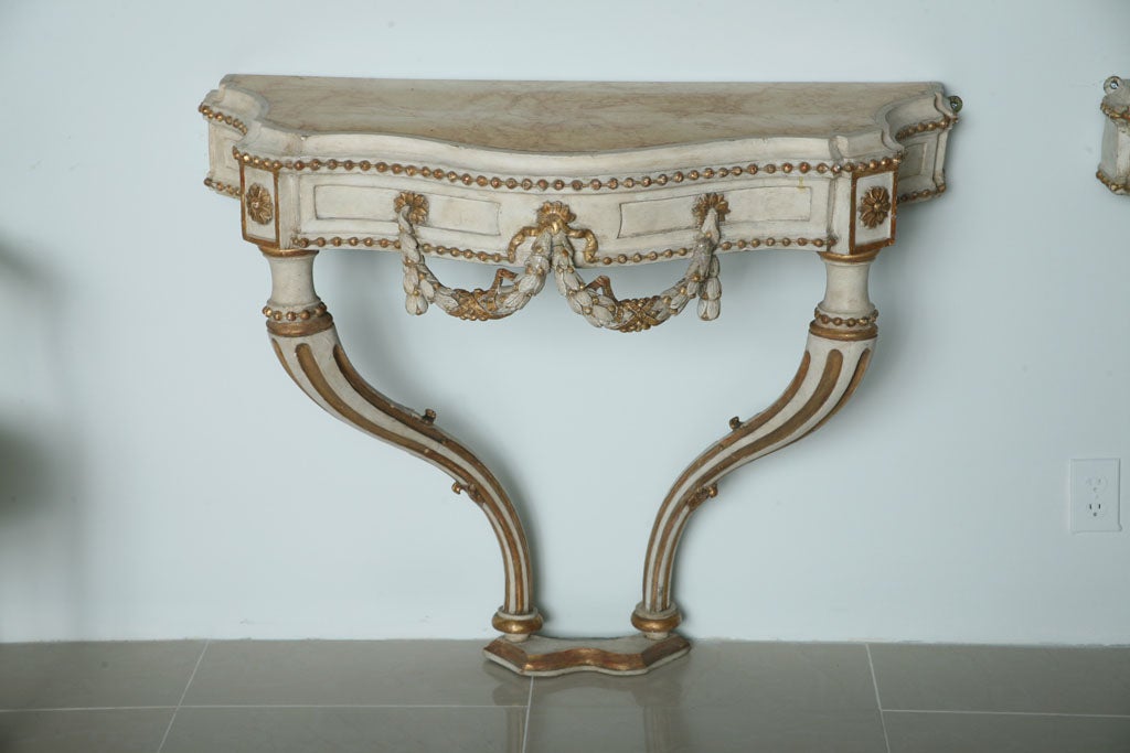 The simulated marble-top over a canted frieze decorated with carved rosettes, foliate, swag and bellflowers, painted cream with parcel gilding, on fluted cabriole legs, joined by a stretcher.