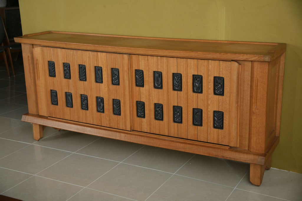 The rectangular top above two sliding ribbed doors with curved ends, each with inset parcel ebonized lozenges decorated with leaf motif, the whole resting on block feet with geometric cutouts.