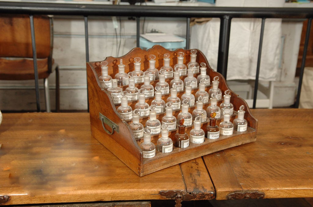 Wooden Apothecary Cabinet with 5 ascending shelves holding 35 pharmacy bottles. The cabinet has two metal handles and a small hidden compartment.
