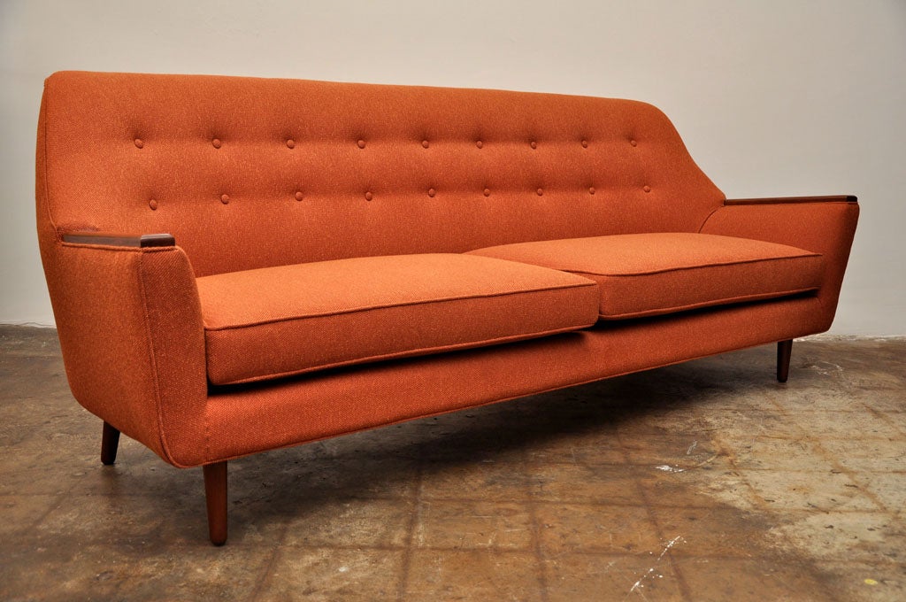 Set upon a walnut frame and four wooden tapered legs, this roomy rust color couch has two large removable cushions and wooden arm rests.