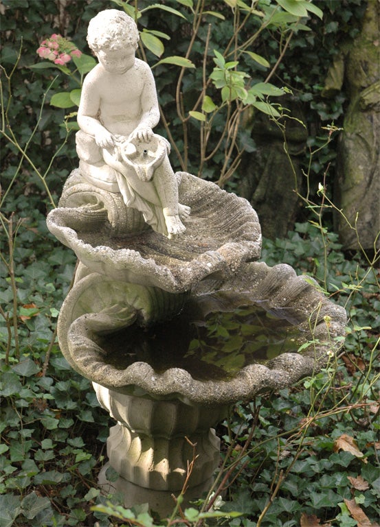 American fountain made in cement of a child pouring water on to two tiers of shells on a scalloped pedestal base.

Four pieces: Top piece of a child figure pouring water on to the second piece of a smaller shell which sits on a third larger shell,