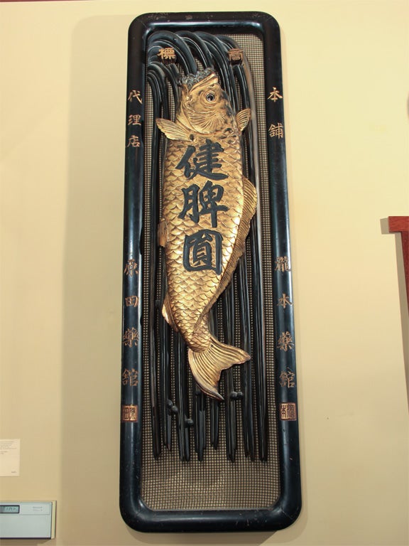 An important and extremely large Japanese kanban or shop sign, of carved wood with a design in black and gold lacquer of a carp leaping up a waterfall, the eye inlaid in glass. Carved and lacquered in gold with the following: 