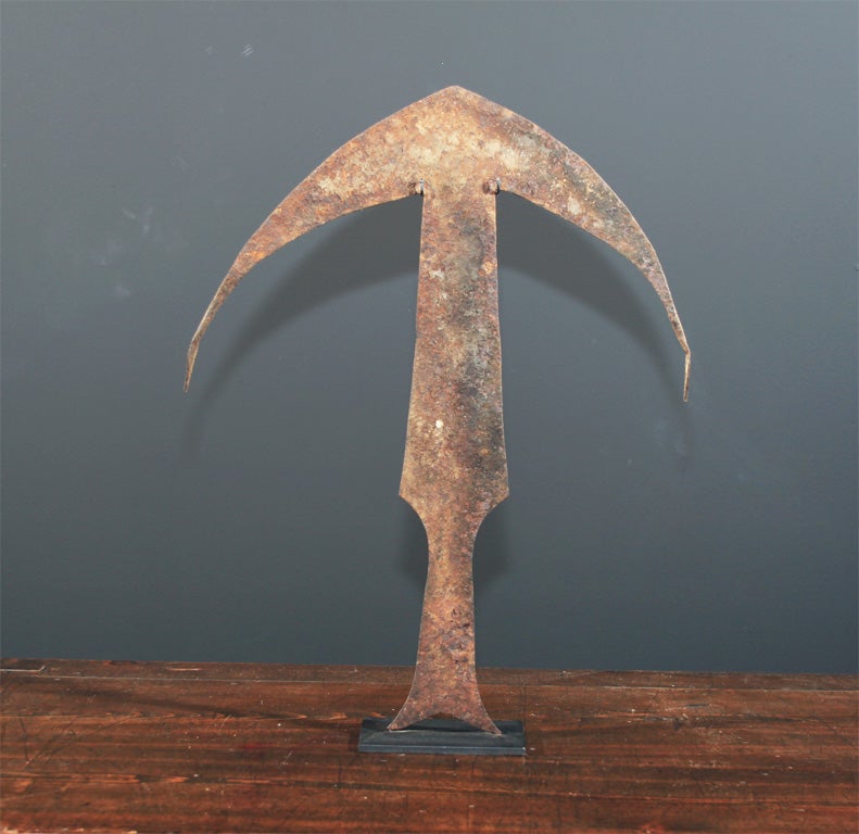 African iron currency form from the Kwele people of Gabon. The large currency with a base of fish tail form and the top with extended wing tips with twisted ends. Mounted on a custom metal stand.