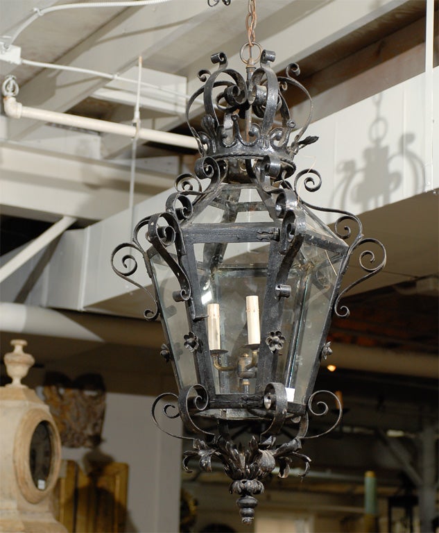 Une exquise lanterne française de grande taille en fer forgé et en verre à trois lumières, surmontée d'une couronne en fer. Cette lanterne hexagonale française du milieu du XXe siècle présente un élégant décor de volutes, de feuilles d'acanthe dans