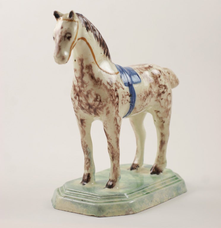A rare and fine English creamware figure of a standing horse with molded saddle, decorated in underglaze oxide colors