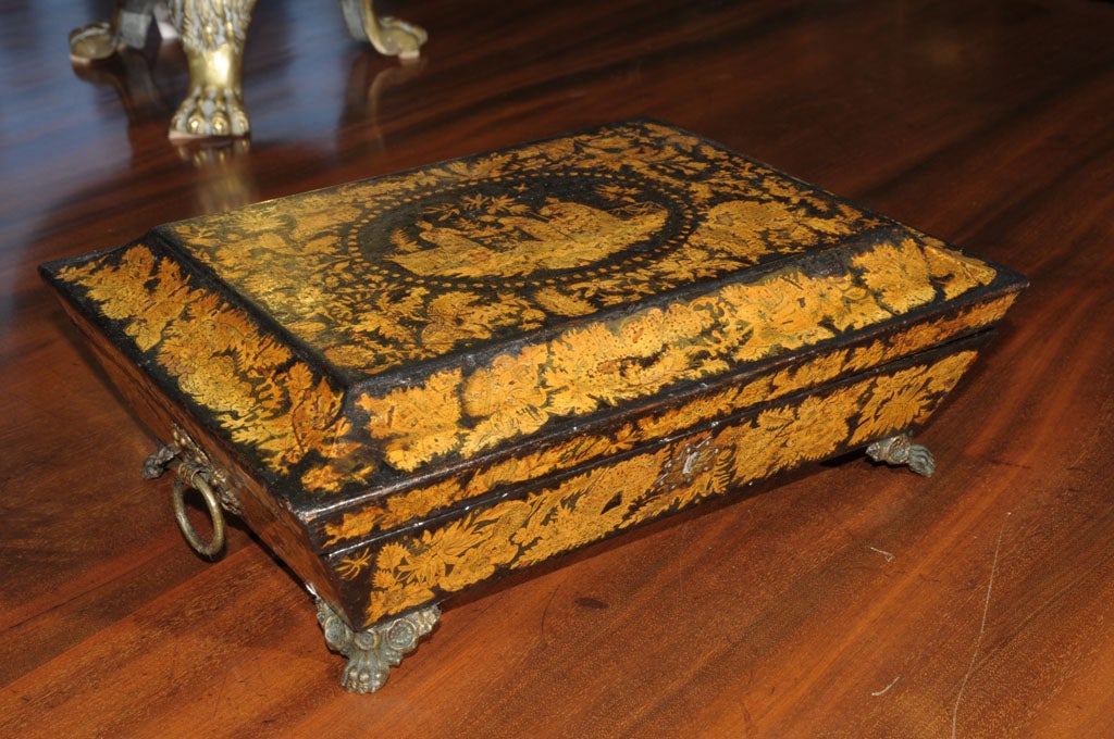 A handsome Regency-era penwork box featuring a Chinoiserie design on the top and sides and resting on foliate-cast brass paw feet with brass escutcheon and accents. The interior lined with a fuchsia-colored paper.<br />
<br />
The Dictionary of