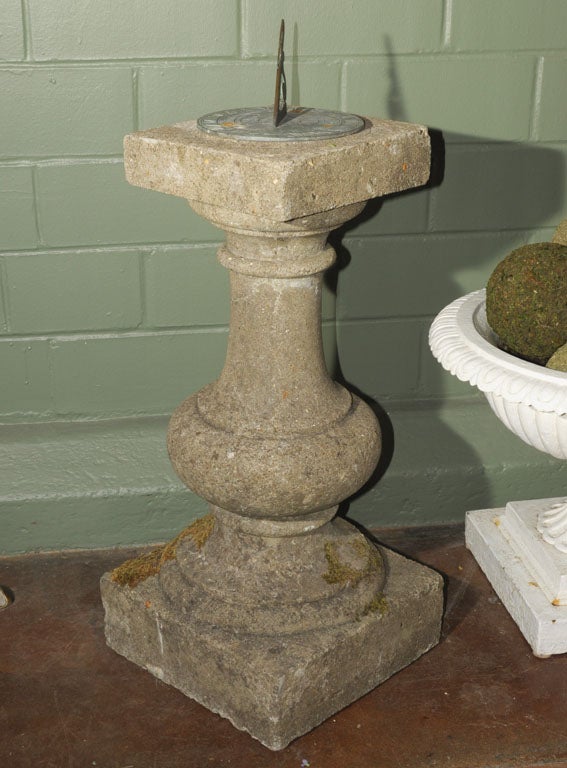 An English sundial of composition or garden stone with bronze dial. Featuring a bronze sundial inscribed with Roman numerals, cardinal directions, and the following quote: 