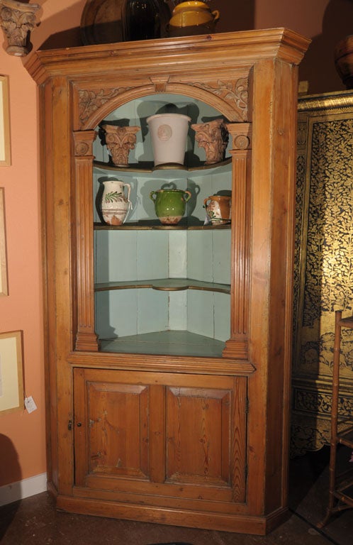 A fine English corner cupboard or display shelving cabinet of patinated pine from the Georgian Era, featuring crown moulding, a moulded column arch with decoratively-carved keystone, scroll-work foliage and rosettes over two carved columns housing