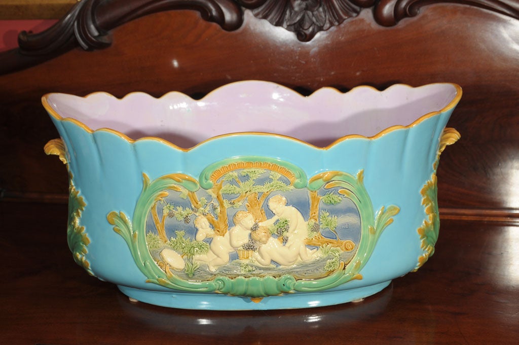 A handsome Majolica jardiniere or wine cooler by the celebrated pottery firm, Minton, featuring a lovely robin's egg blue exterior on an oblong body with accents of yellow gold around the scalloped top edge, molded in relief on opposing sides with