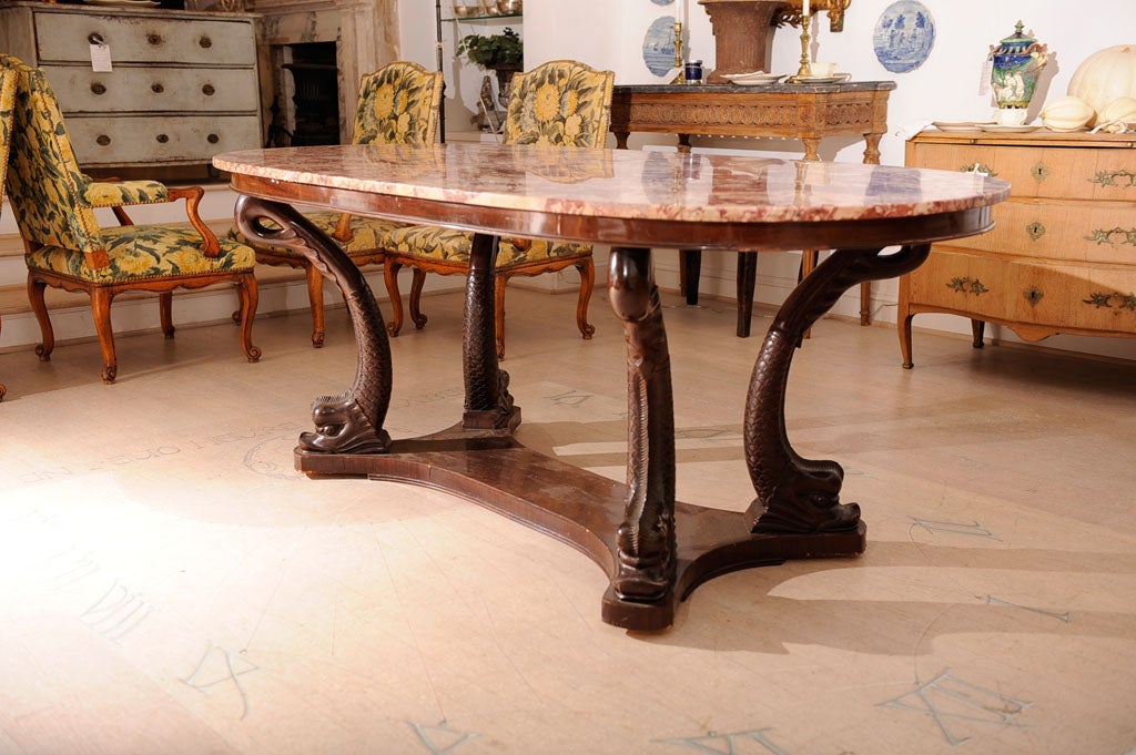 An Italian oval dining table with rose marble top with carved mahogany dolphin motif decoration base.