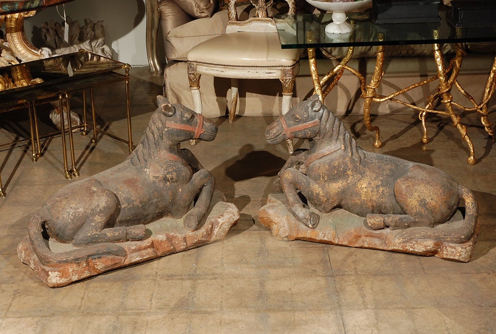 A pair of polychrome decorated carved hardwood models of recumbent horses each wearing harness on naturalistic base. Beautiful patina with slight gilt remaining.
