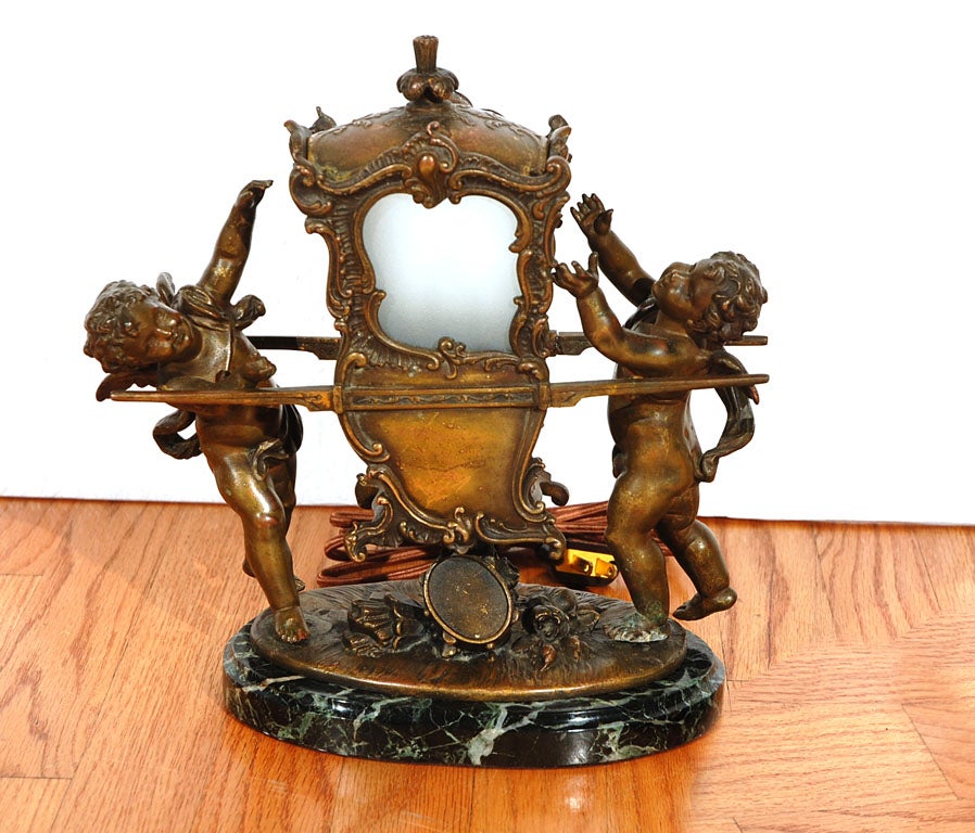 Single light in a carriage carried by two cherub fugures. A charming spelter light with bronze finish, fine detailing to the cab and the figures with their flowing garlands. Portions of thefrosted, glass windows replaced, and minor repairs to the