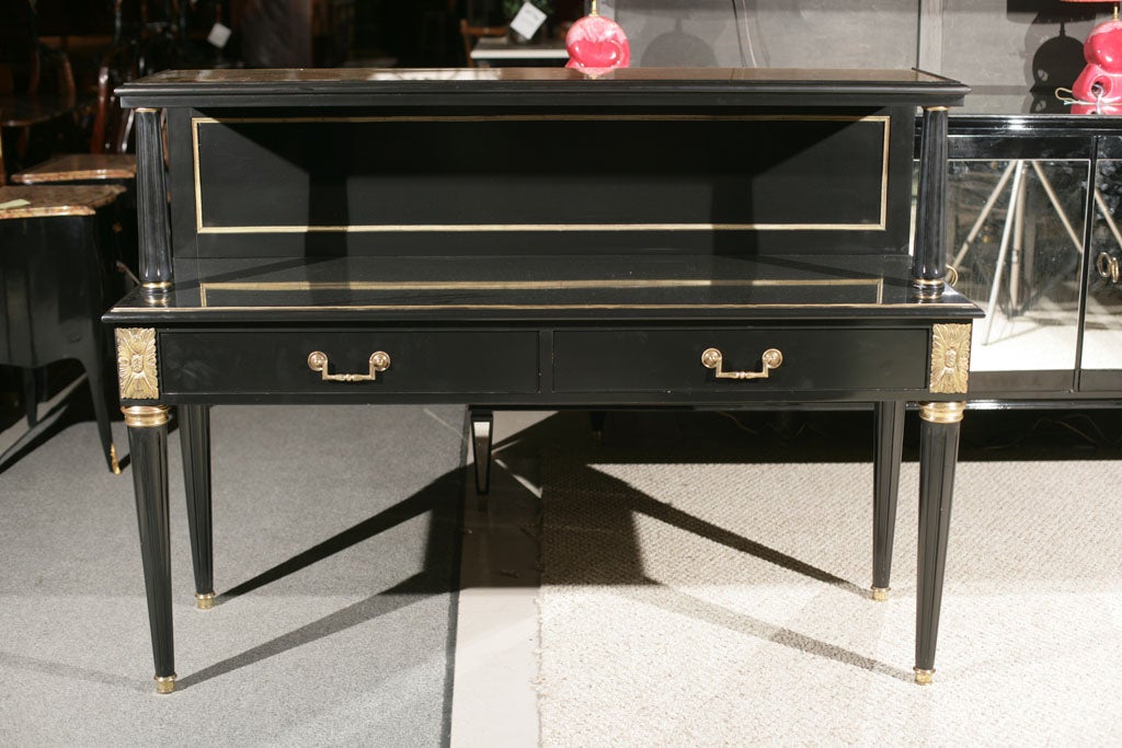 An one-of-a-kind server, circa 1930s, thoroughly ebonized, the upper tier with verre églomisé top connected with a rectangular bronze banded back splat, supported by two fluted columns, over two drawers with custom interior fitting, standing on