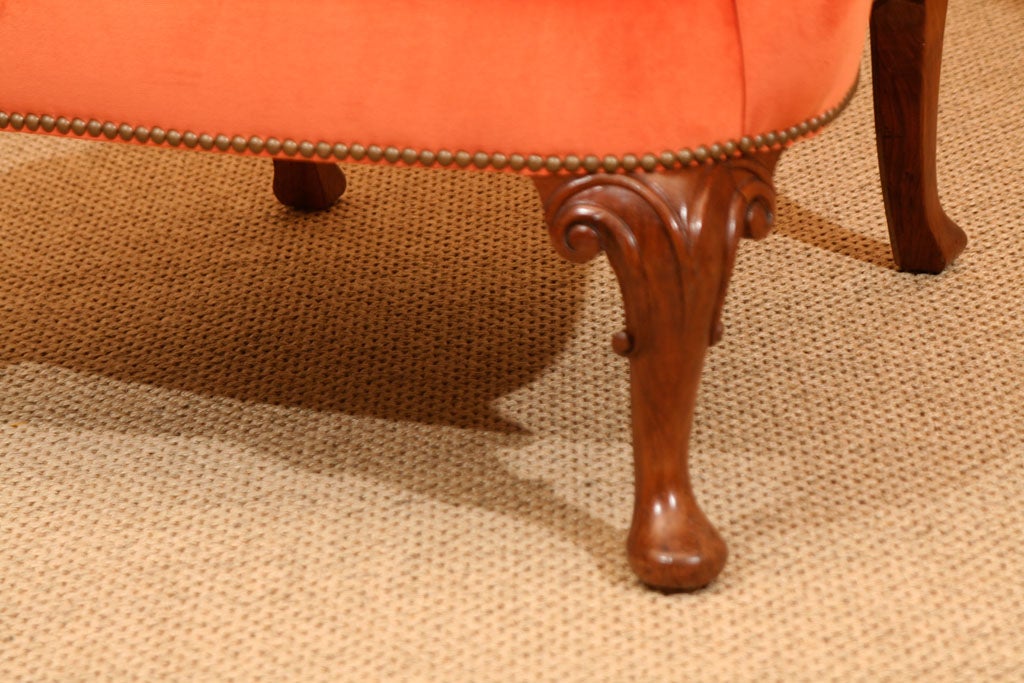 A late 19th century walnut wing armchair on moulded cabriole legs with carved knees on pad feet upholstered in orange cotton velvet and hand loomed pink and orange silk Ikat with nailhead trim.
  