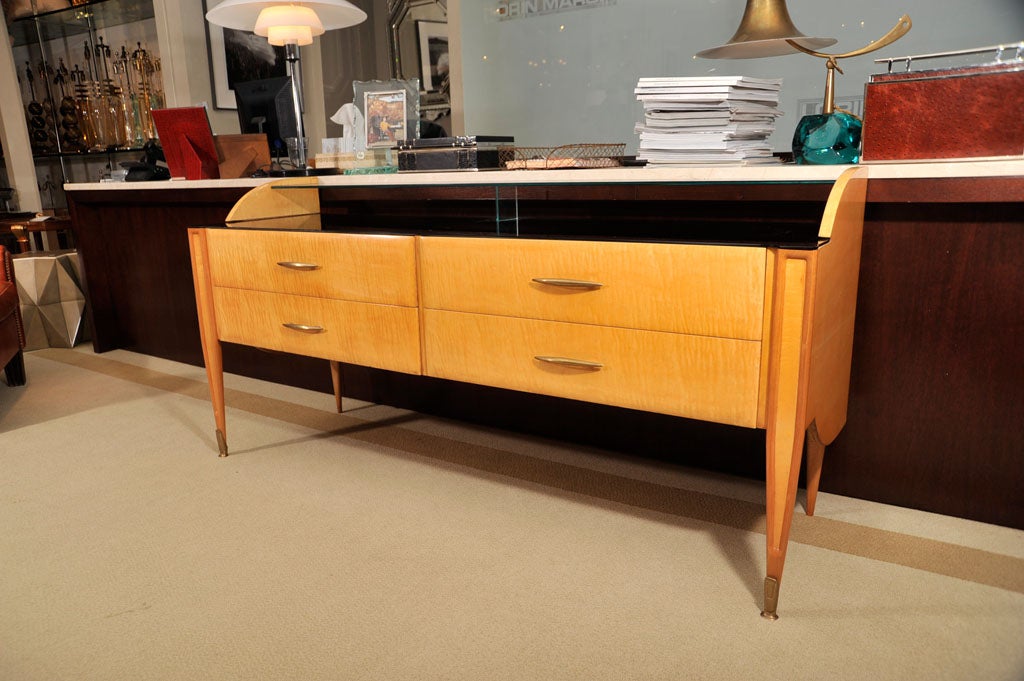 Sycamore console with raised glass shelf, black glass top, four-drawers with bronze bateau pulls, sculpted bronze sabots.