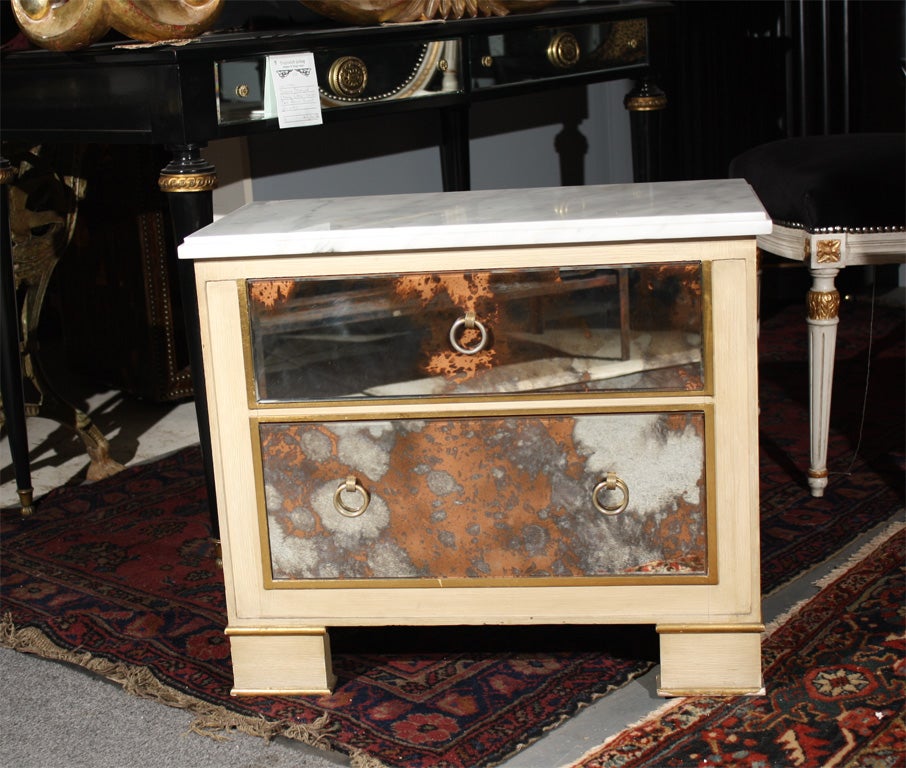 Pair of cream painted and smoke glass front marble top nightstands with two drawers. Standing on block feet.