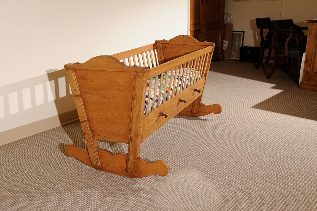 A lovely cradle featuring scalloped, tapering headboard and footboard ending in decoratively shaped rockers. Fixed, gated sides with three hand-carved rocking pegs.