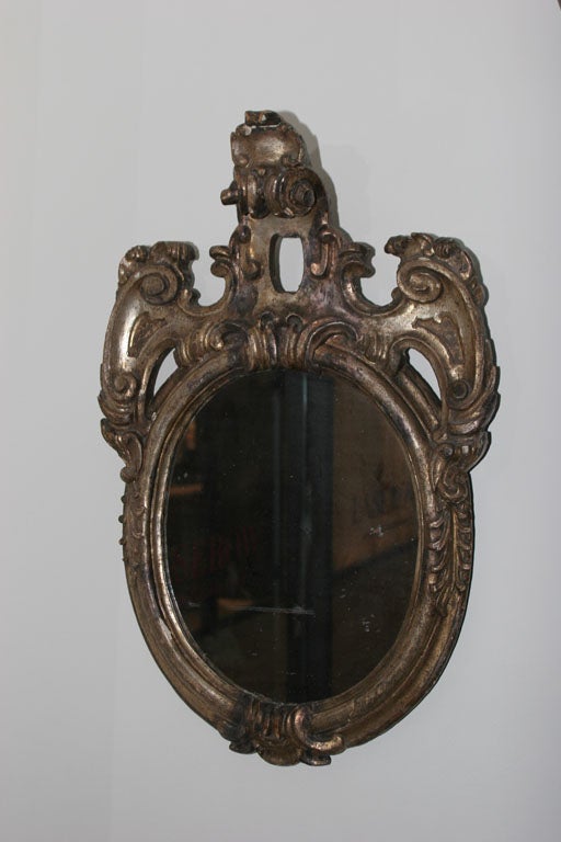 Mirror Oval Italian Baroque Period 18th Century Italy. An unique wall mirror made during the Baroque period 1650-1720 in Italy. An oval frame decorated with carvings in a silver leaf. Original mercury mirror glass.