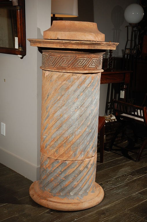 A cylinder column base terra cotta stove with a round top over a greek key motif and diagonal fluting down the body. A round molded edge forms the base. This terra cotta piece makes an elegant pedestal or garden plant stand.