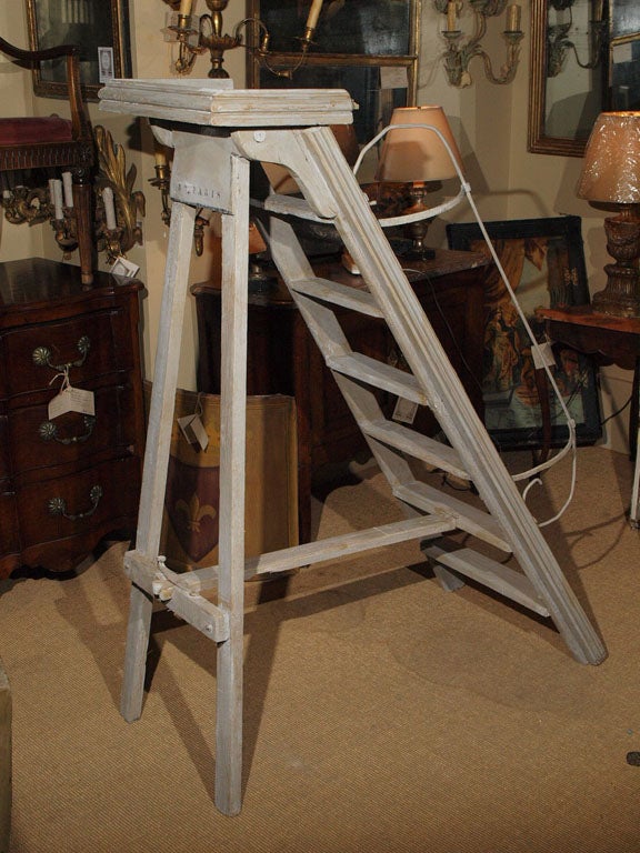 French gray painted wood ladder.  The 6 step ladder has an iron railing on the left side.  The closing mechanism consists of a sliding metal bar to unlock the extension, which then pivots on a wood dowel.  The platform at the top is of a more recent